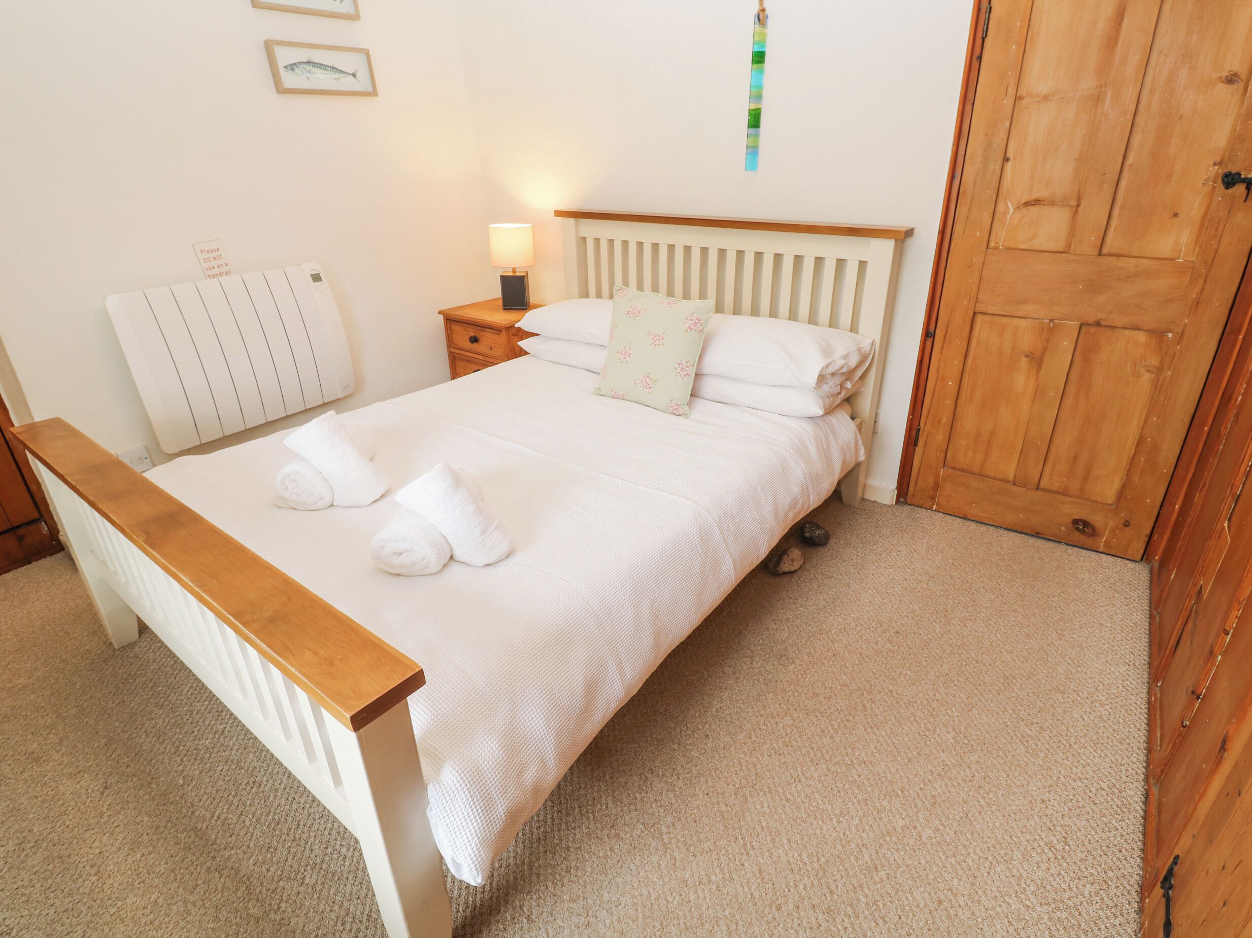 A neatly made bed with white linens and two towels, a bedside table with a lamp, a wooden headboard, and a wooden door.