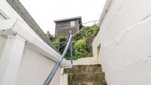 Un escalier étroit avec une rampe bleue mène à un bâtiment à l’architecture moderne.