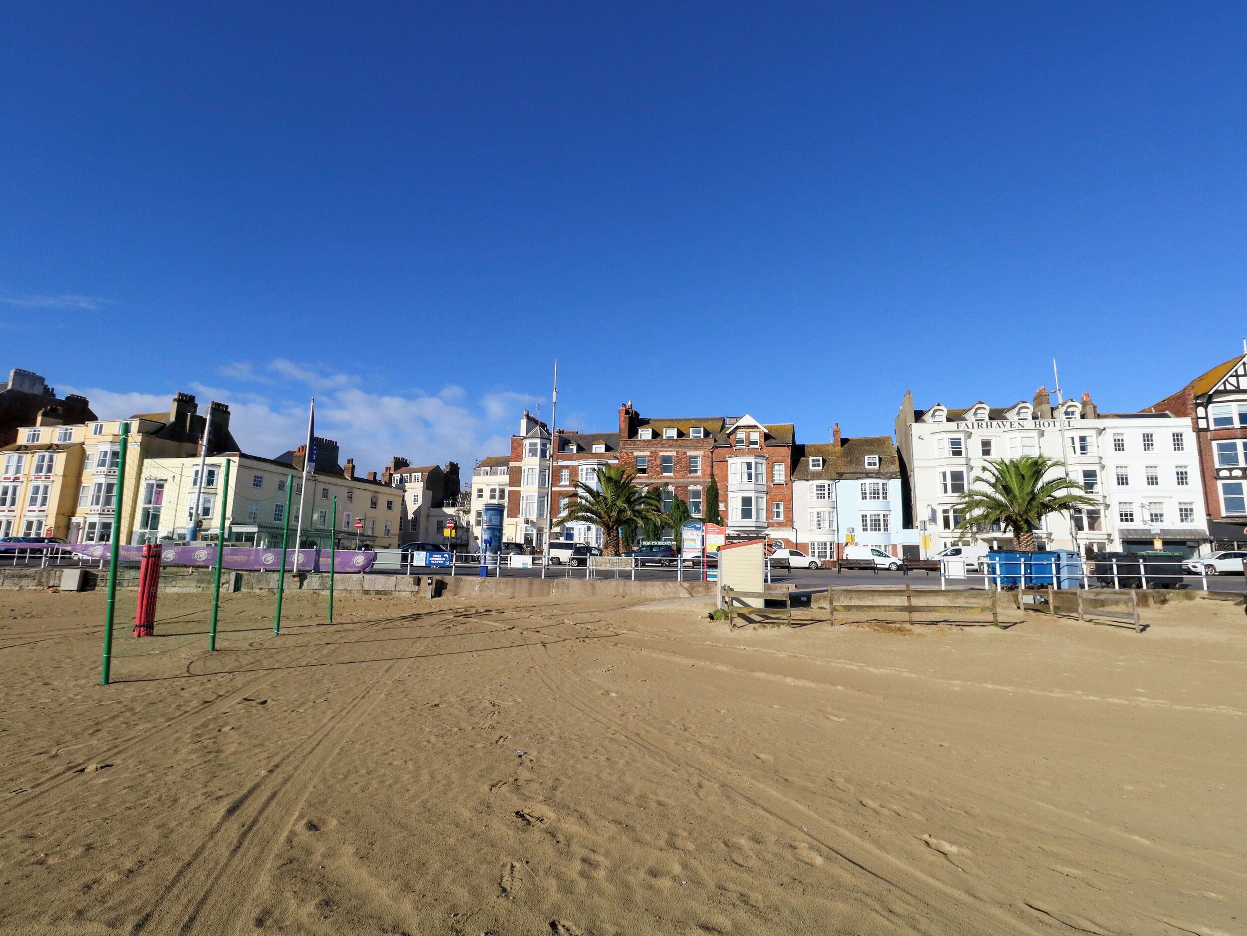 A beach with a sandy area and a row of buildings in the background, including a hotel named 'Fairhaven Hotel'.