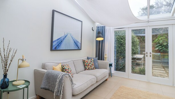 A modern living room with a sofa, a framed picture, a lamp, and a view through a glass door. - 6 Inveravon (Christchurch)