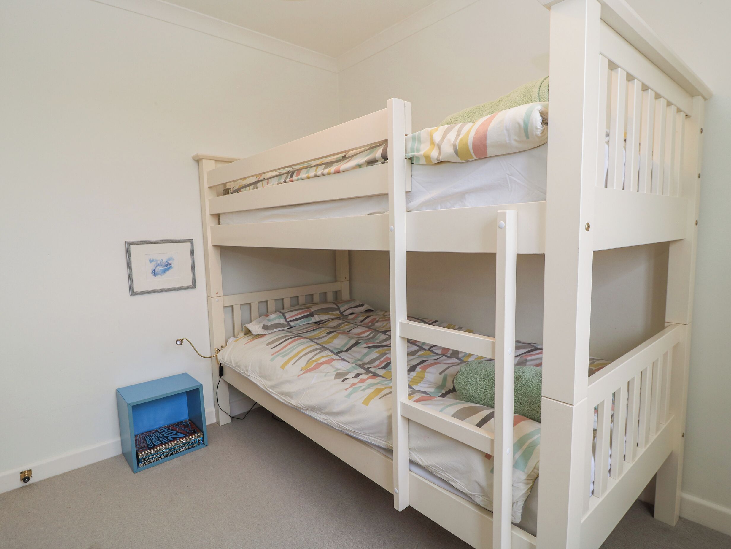 Habitación con literas, un caja azul para guardar cosas y un cuadro en la pared.