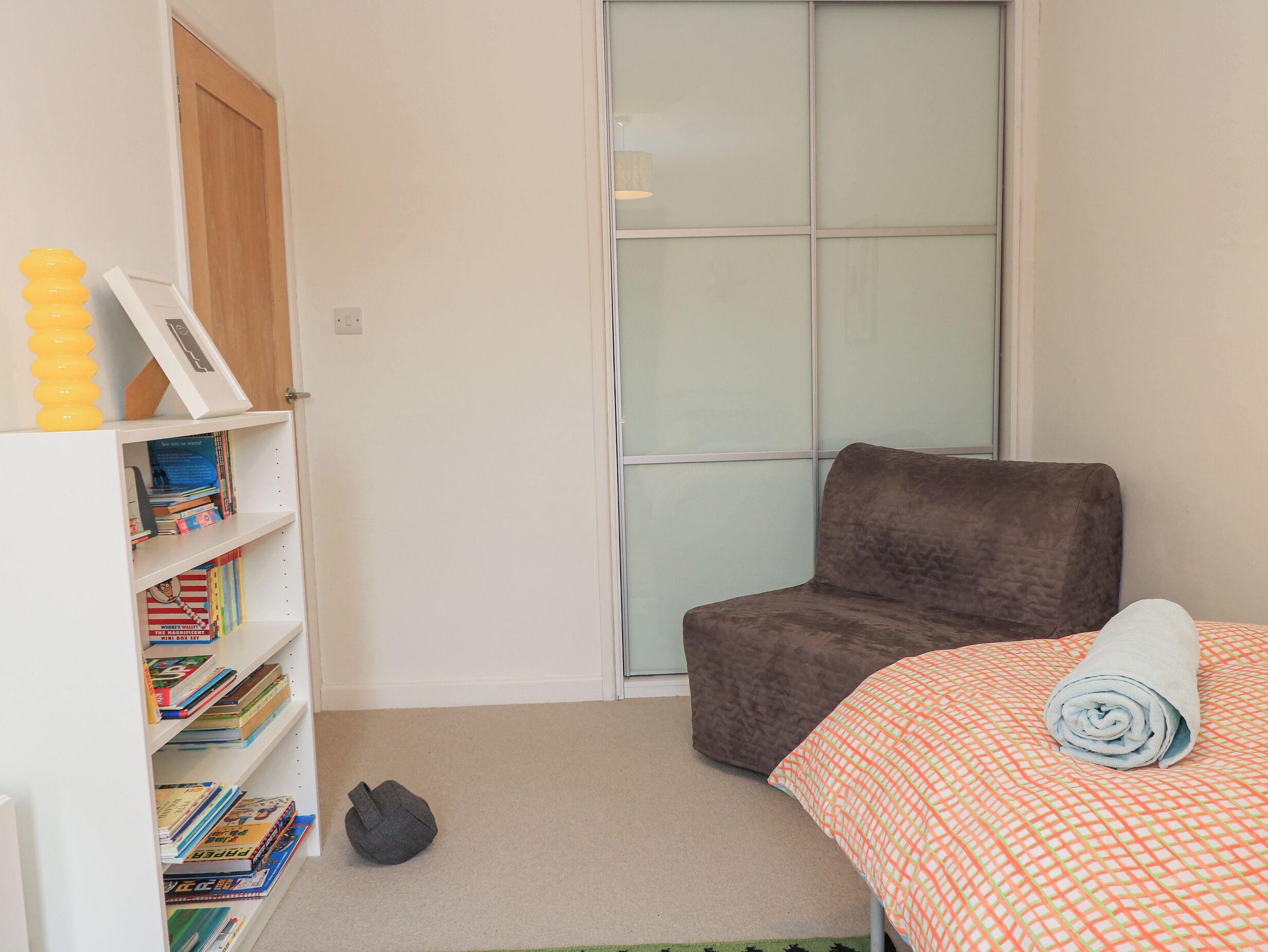 Een slaapkamer met een bed, een stoel, een boekenkast en een raam.