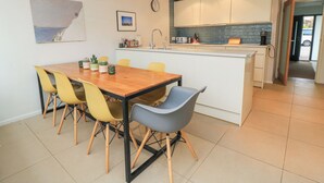 A modern kitchen with white cabinets, a built-in island, and a dining area with a wooden table and yellow chairs. - 6 Inveravon (Christchurch)