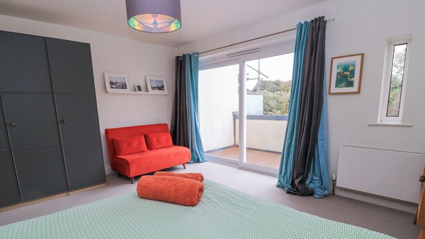 A bedroom with a bed, a red sofa, a wardrobe, and a window with curtains.