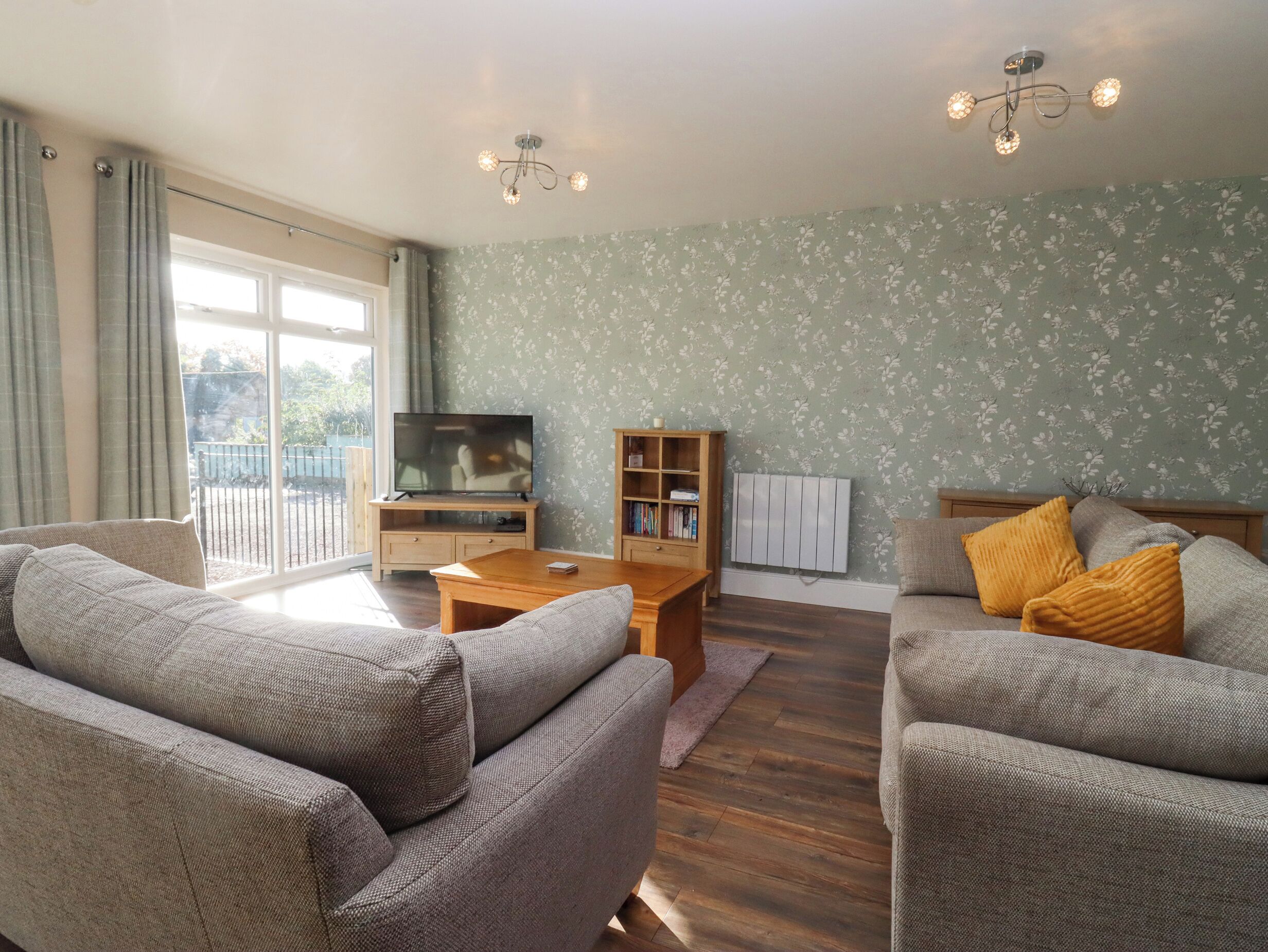A living room with two sofas, a coffee table, a TV on a wooden stand, a bookshelf, and a radiator.