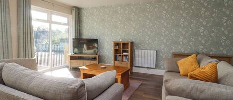 A living room with two sofas, a coffee table, a TV on a wooden stand, a bookshelf, and a radiator.