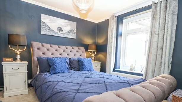 Un dormitorio con una cama grande, dos mesitas de noche, una mesita auxiliar, una ventana con cortinas y una obra de arte colgada en la pared.