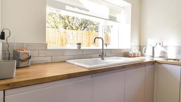 Een moderne keuken met een houten aanrecht, witte kasten, een inbouwgootsteen en een raam met uitzicht op een houten schutting.