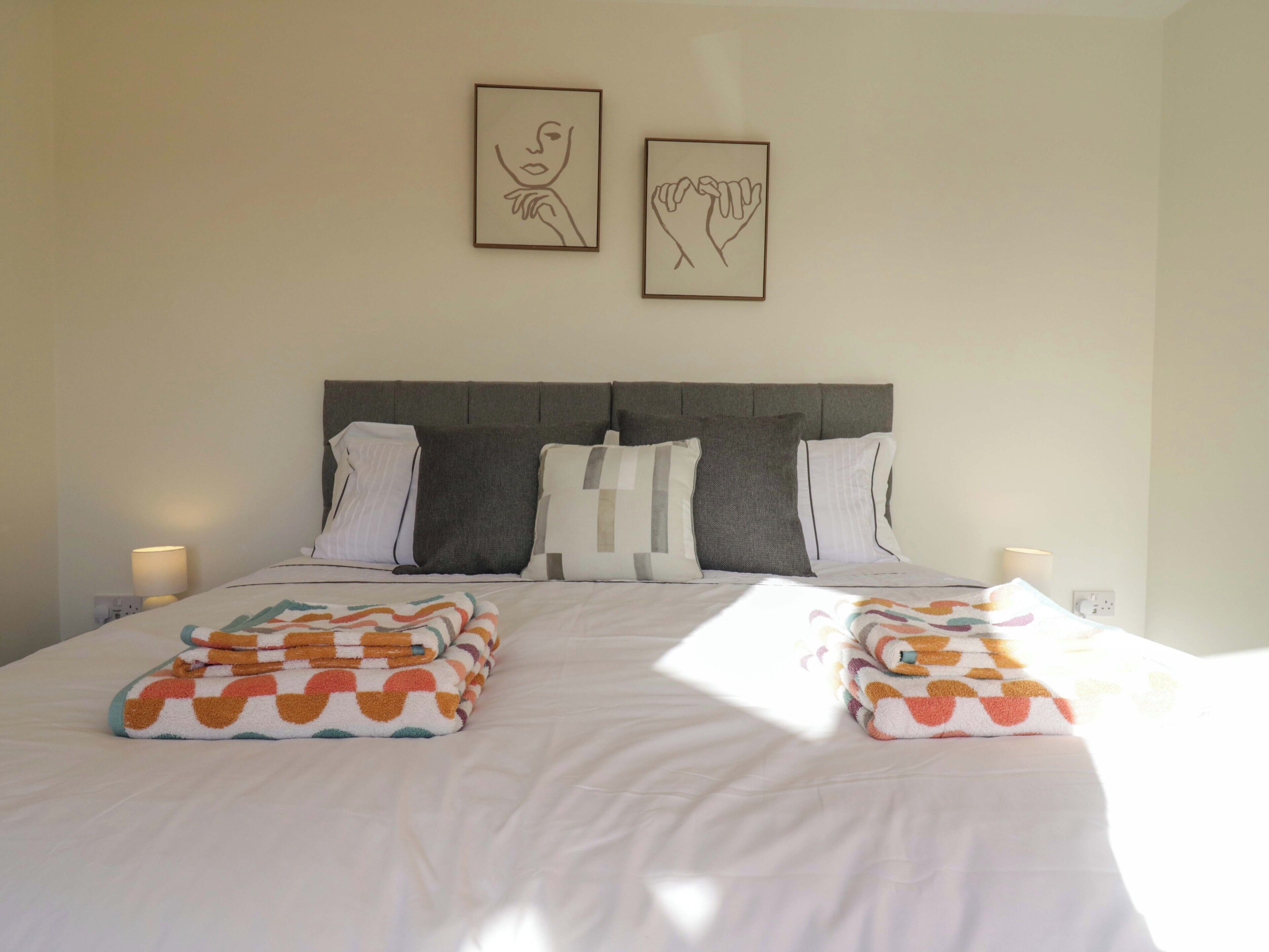 A neatly made bed with two pillows, a headboard, and two wall-mounted artworks.