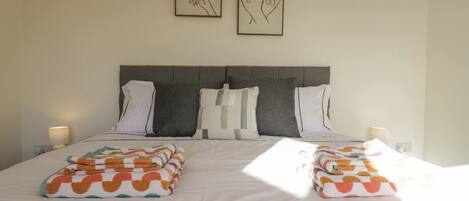 A neatly made bed with two pillows, a headboard, and two wall-mounted artworks.