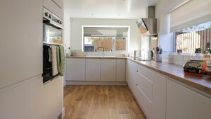 A modern kitchen with white cabinets, a wooden countertop, and a window providing natural light. - Farmer's Rest (Ely)