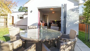 An outdoor patio with wicker furniture and a glass table, a white building with an open door, and a garden area. - Farmer's Rest (Ely)