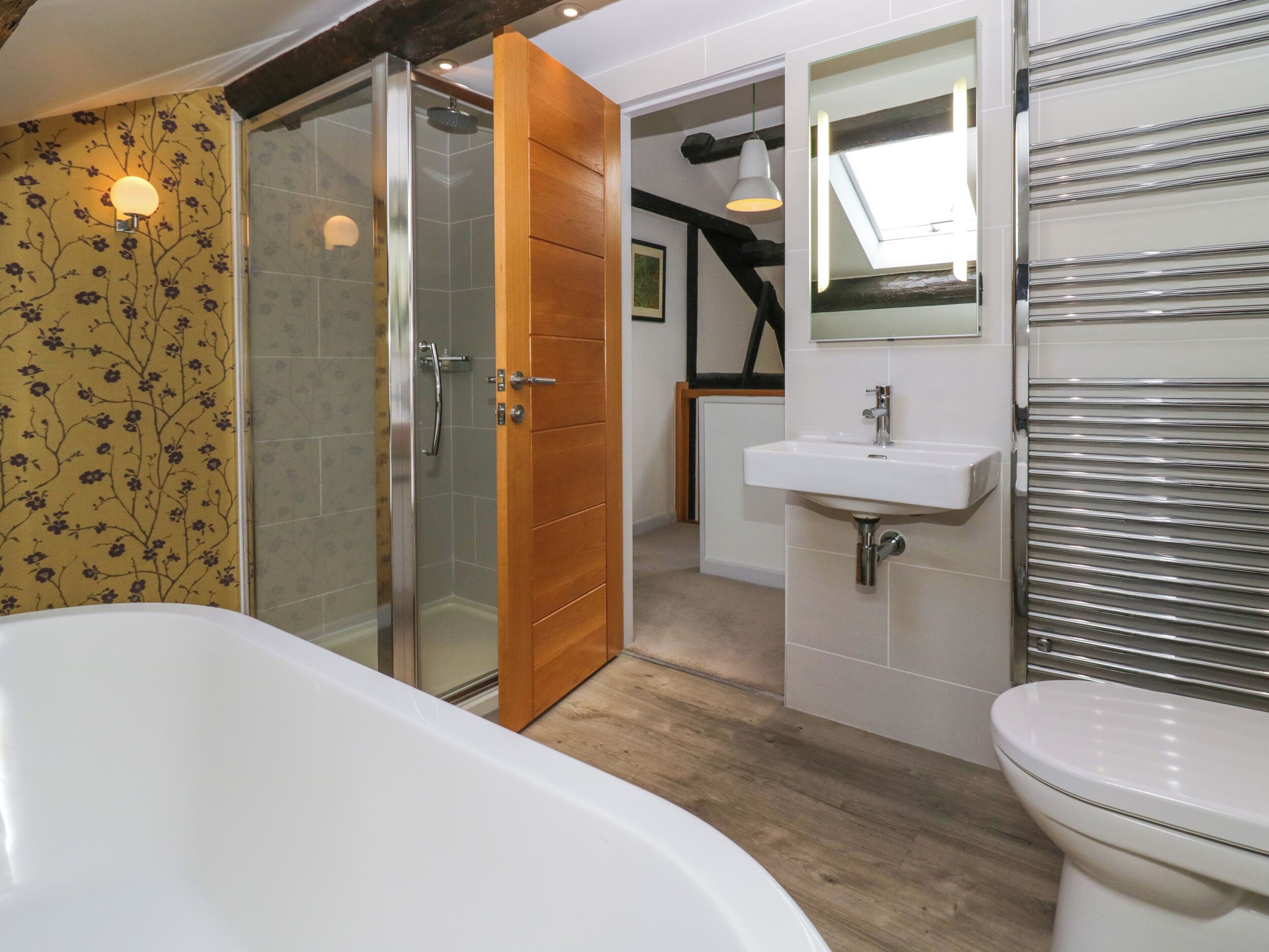 A modern bathroom with a glass-enclosed shower, a wooden door, a white sink, and a toilet.