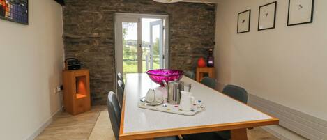 A dining area with a stone wall, a wooden table, chairs, a chandelier, and framed pictures on the wall.