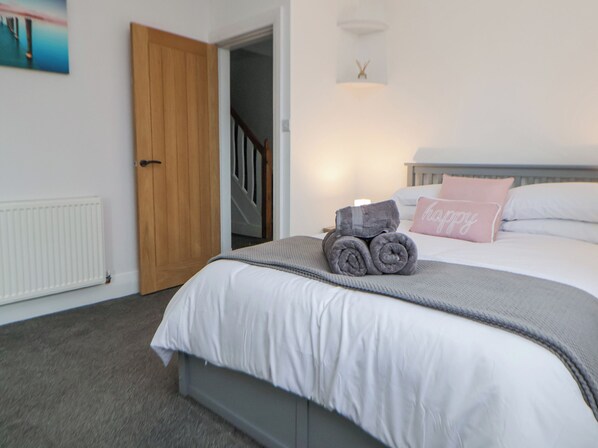 A bedroom with a bed, a rolled-up towel, a pink pillow, a wooden door, and a staircase.