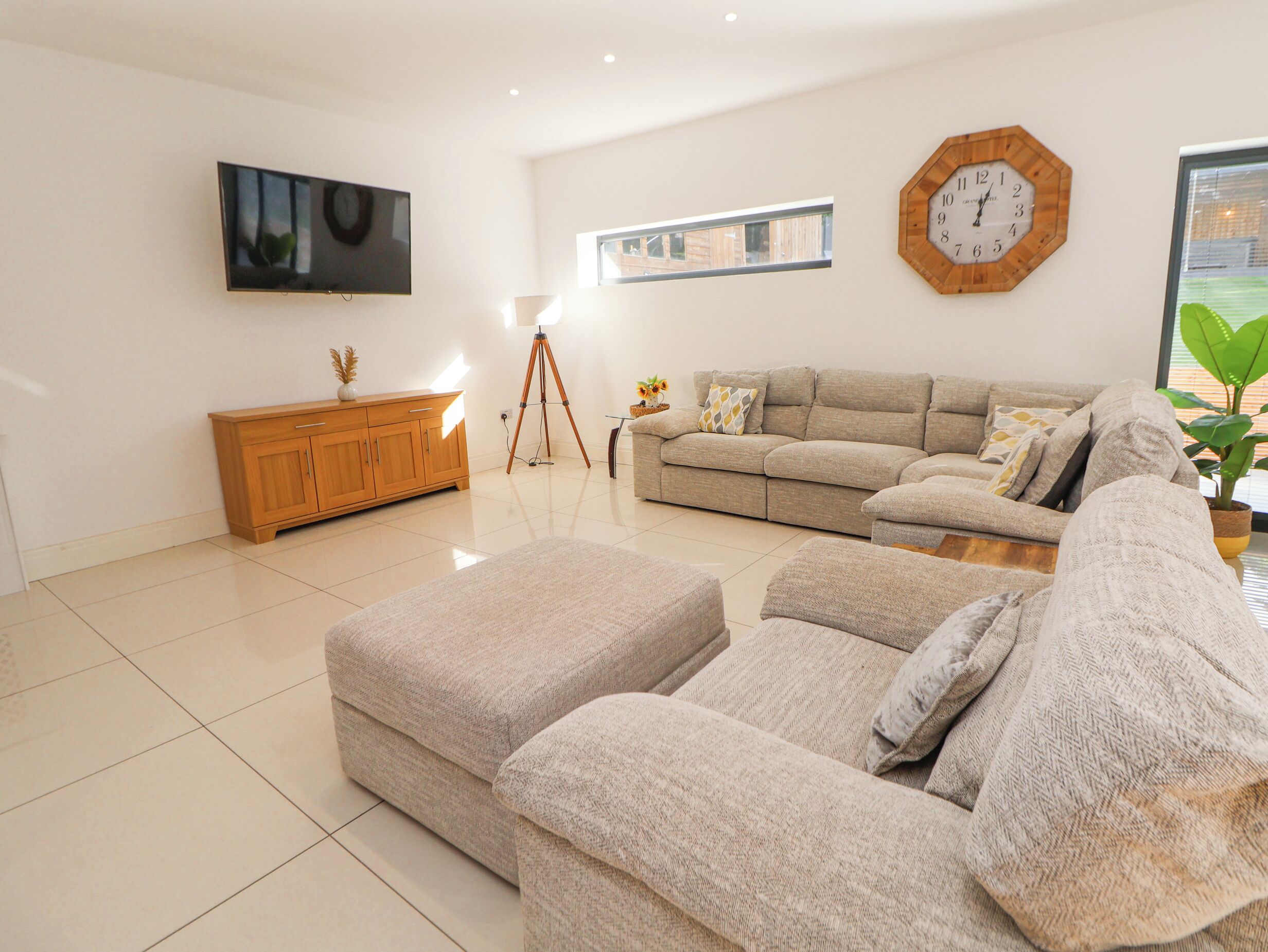 A modern living room with a large sofa, a wooden cabinet, a floor lamp, and a wall-mounted clock.