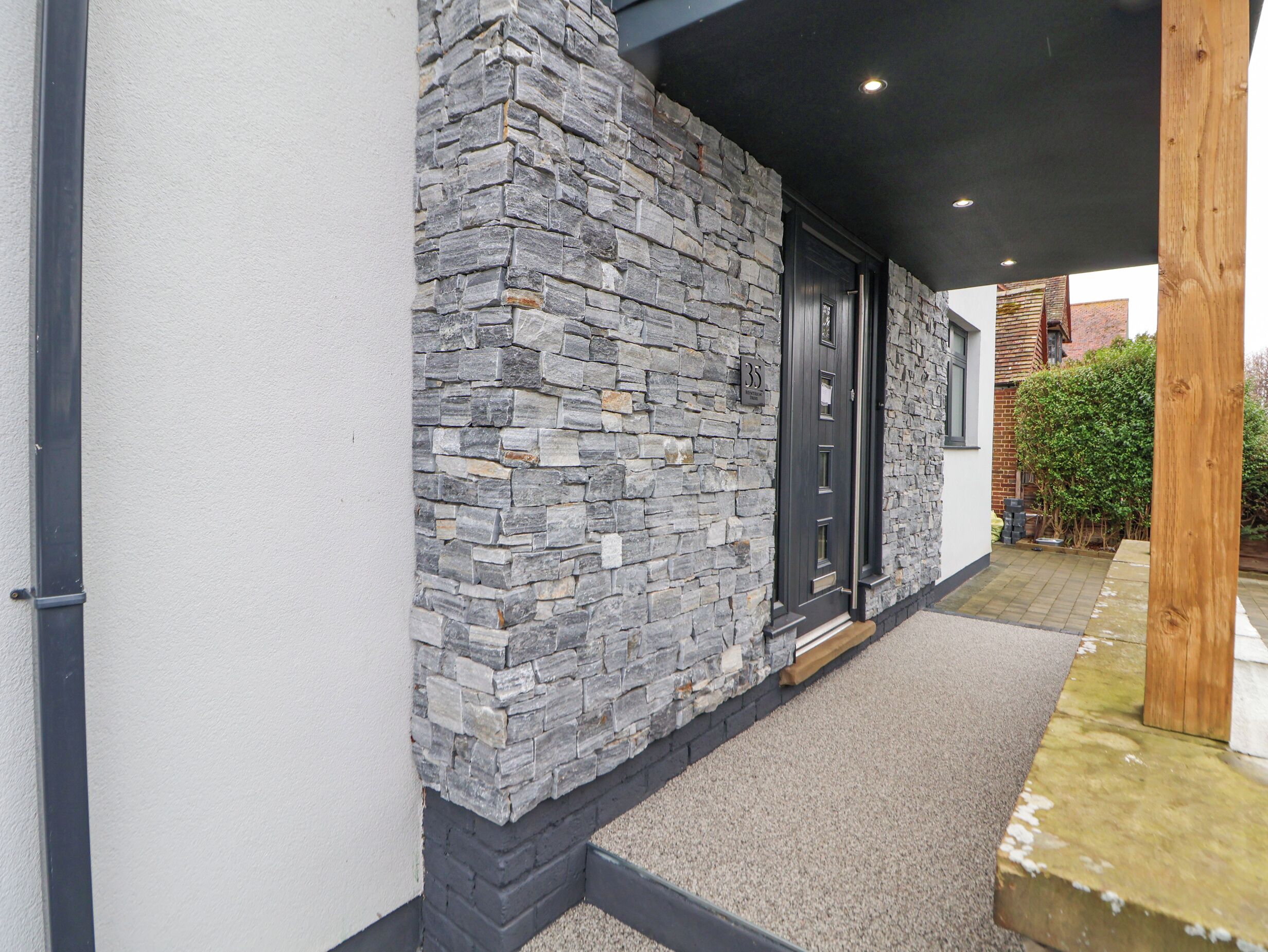 A modern building with a stone facade, a black door, and a small garden area.