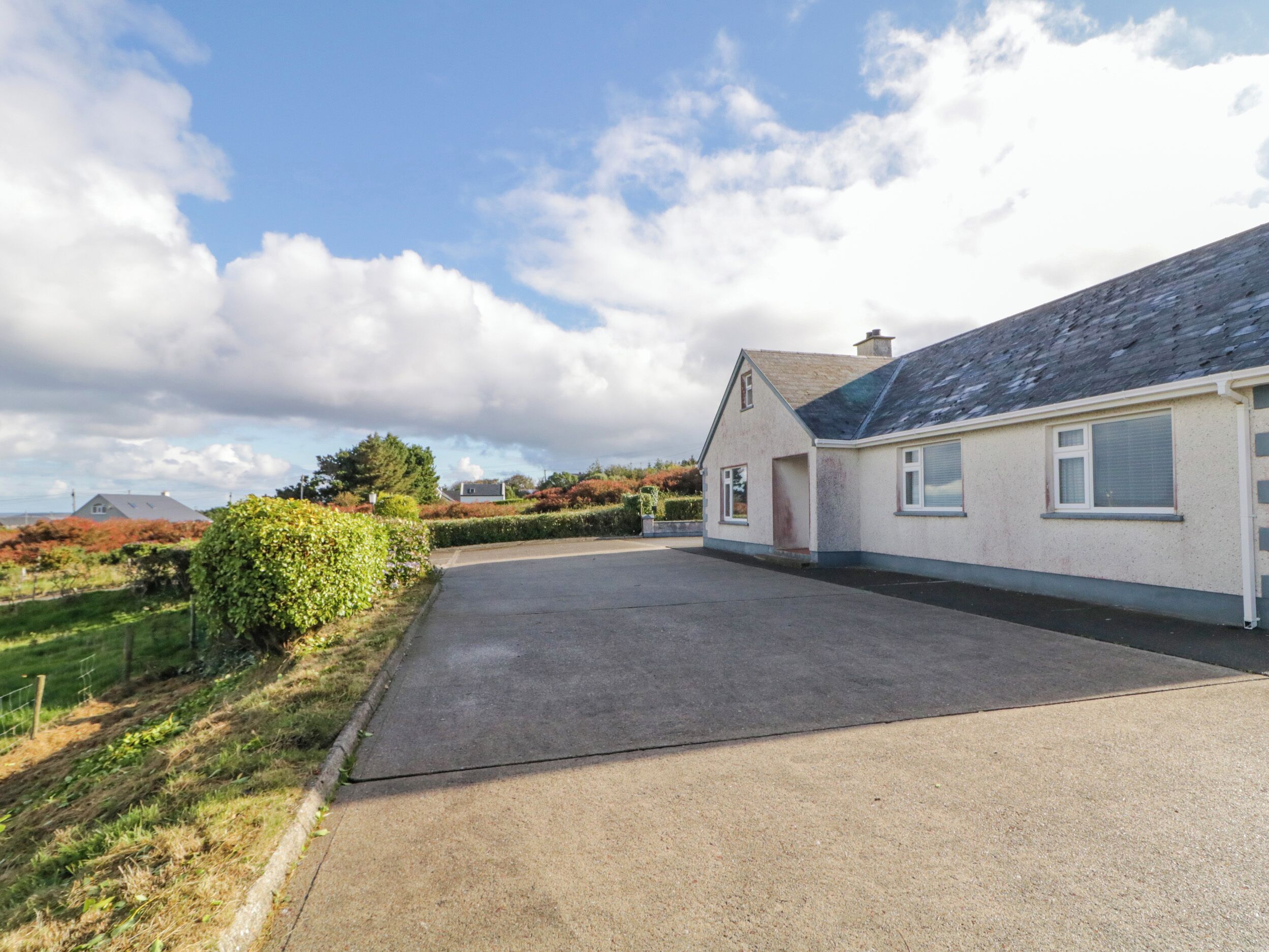 A residential property with a paved driveway leading to a house with a sloped roof.