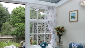 A room with a view of a river, a glass table with a speaker, and a vase with flowers. - Troutbeck Cottage (Ludlow)