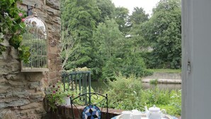 A stone wall with a birdcage, a metal chair, and a table with a tray of white teacups and a teapot. - Troutbeck Cottage (Ludlow)