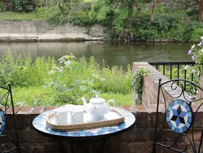 A table with a tray of white teacups and a teapot, set against a stone wall overlooking a river. - Troutbeck Cottage (Ludlow)