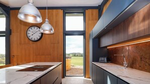 A modern kitchen with wooden cabinets, a marble countertop, pendant lights, and a view of the outdoors. - Brock House (Northallerton)