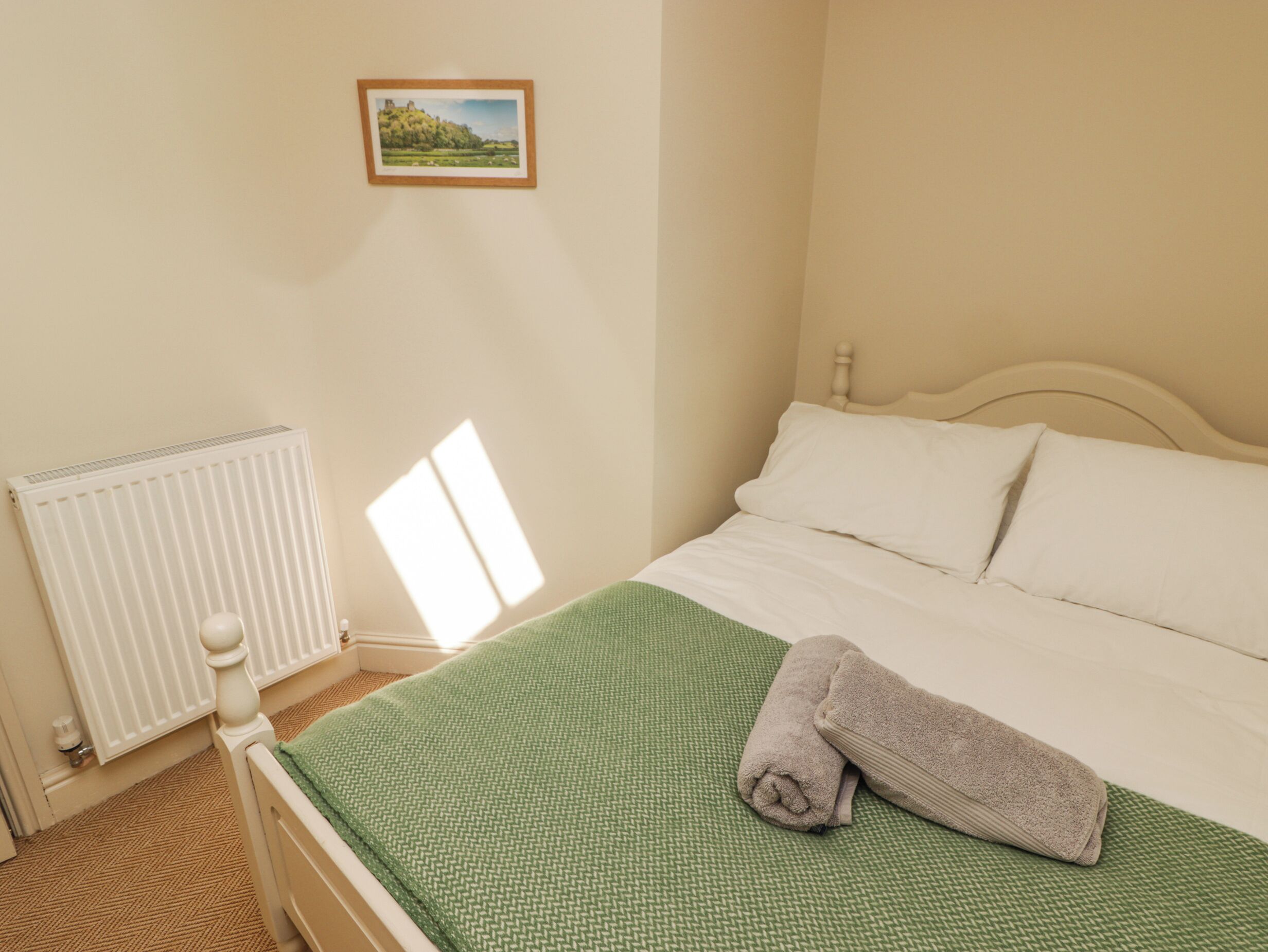 Un dormitorio con cama, un radiador, una ventana y un cuadro en la pared.