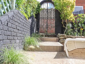 Un jardin rustique avec un mur en briques, un portail en métal et un lit doté d’une tête de lit blanche.