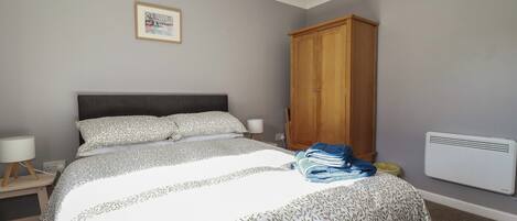 Une chambre avec un grand lit, une armoire en bois, une table de chevet avec une lampe et un tableau encadré au mur.