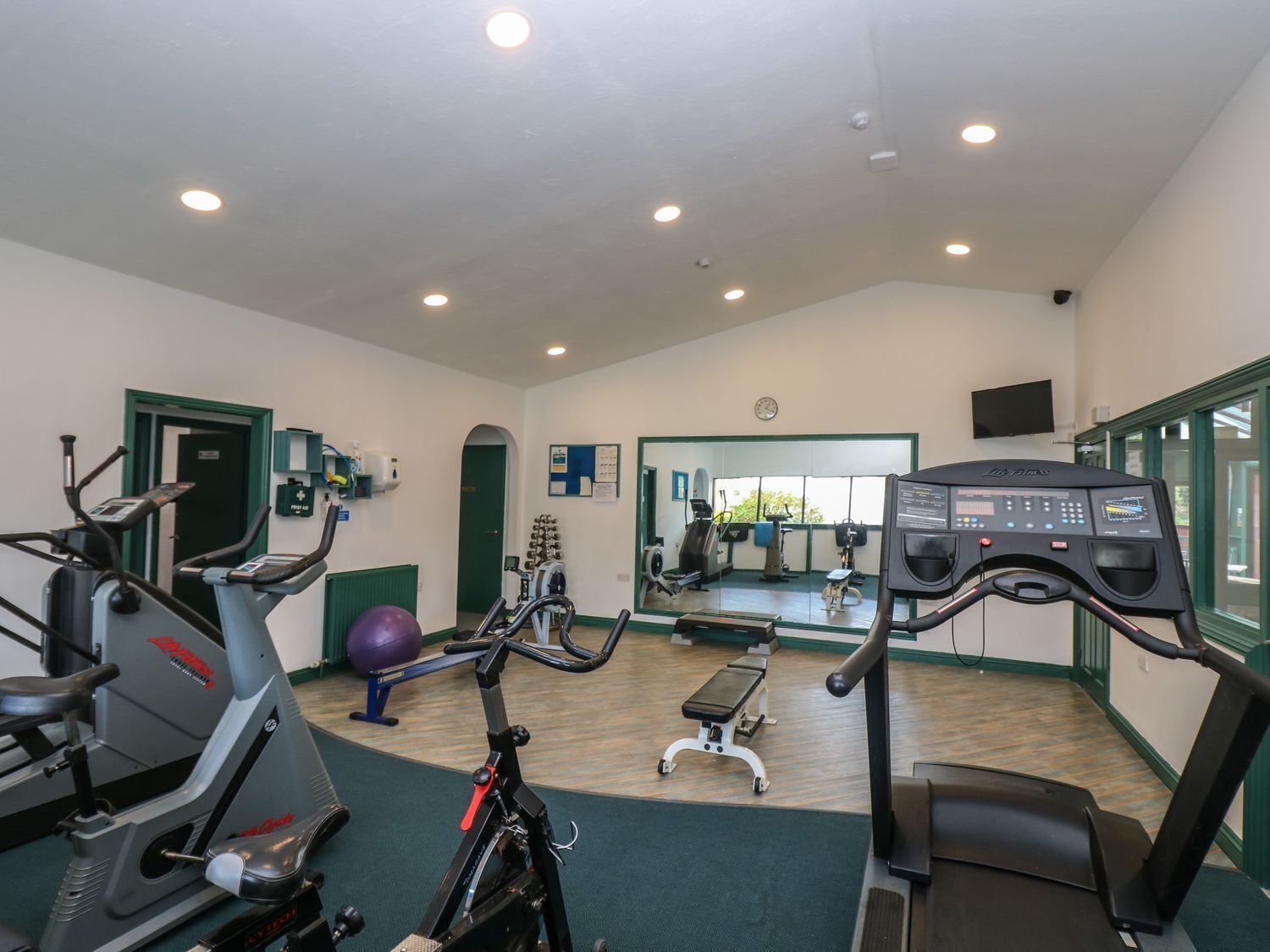 A gym with various exercise equipment, a mirrored wall, and a clock on the wall.