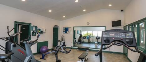 A gym with various exercise equipment, a mirrored wall, and a clock on the wall.