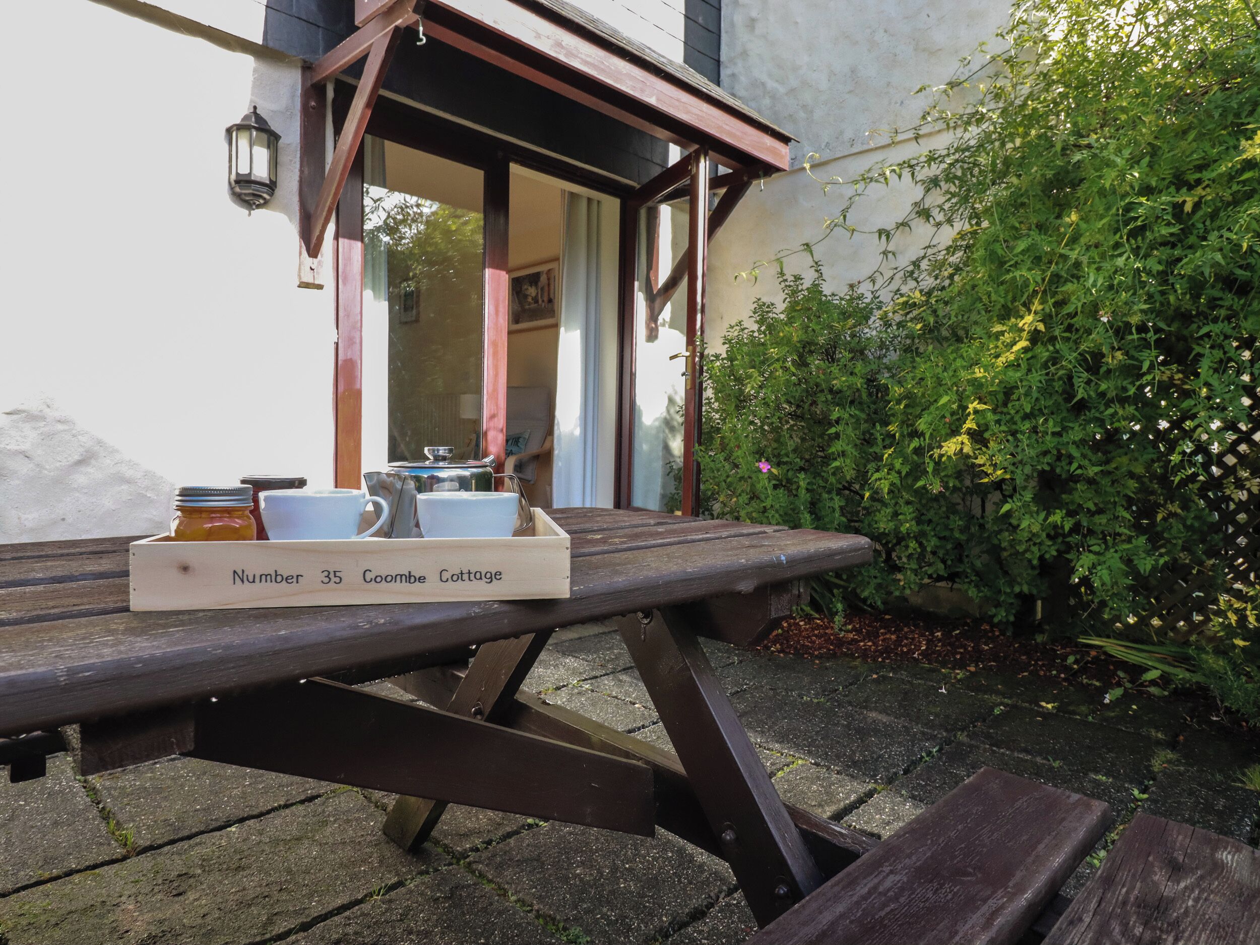 A wooden table with a tray labeled "Number 35 Coombe Cottage" and a lantern on the wall.