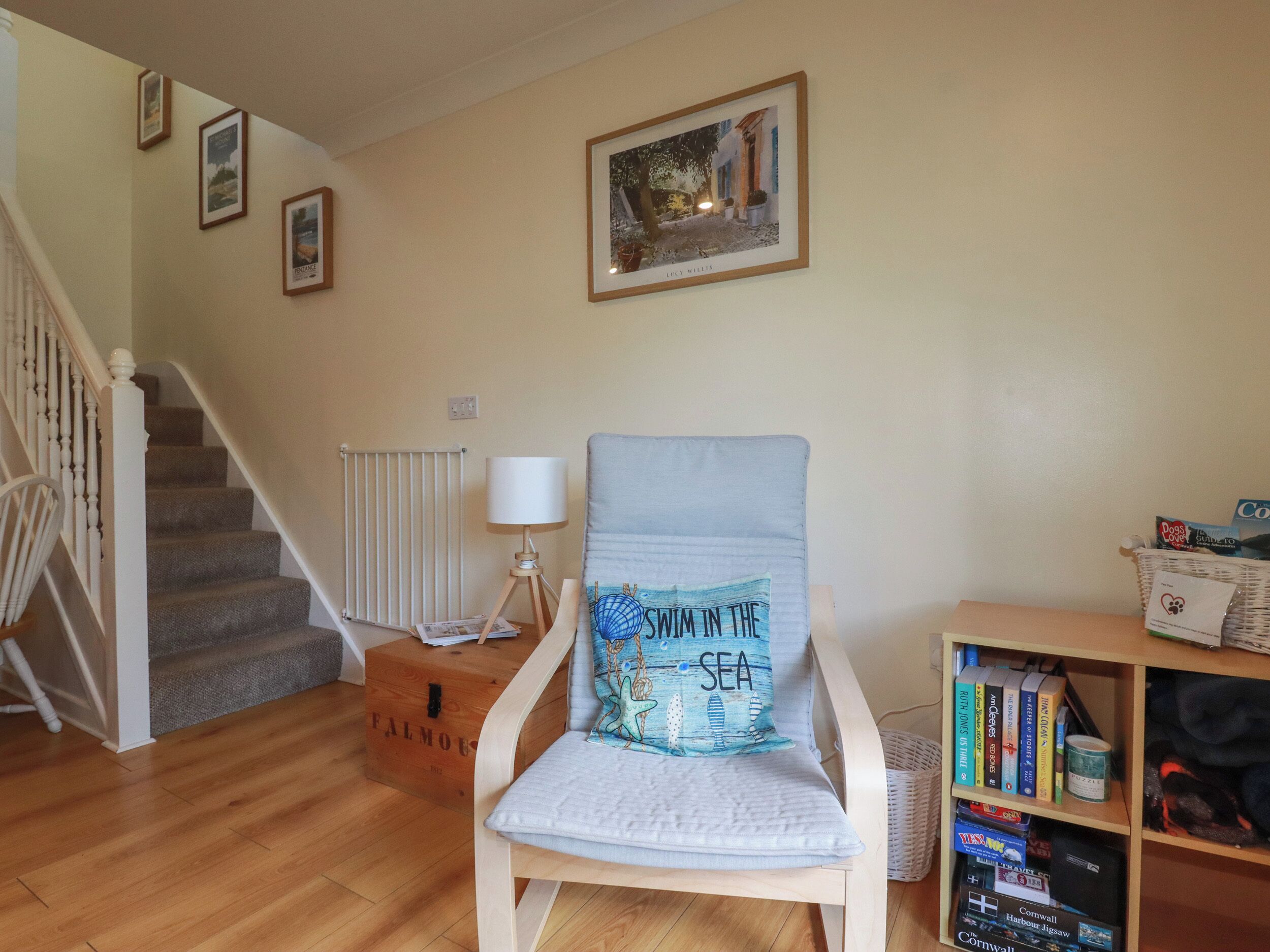A living room with a wooden chair, a bookshelf, a framed picture on the wall, and a staircase.
