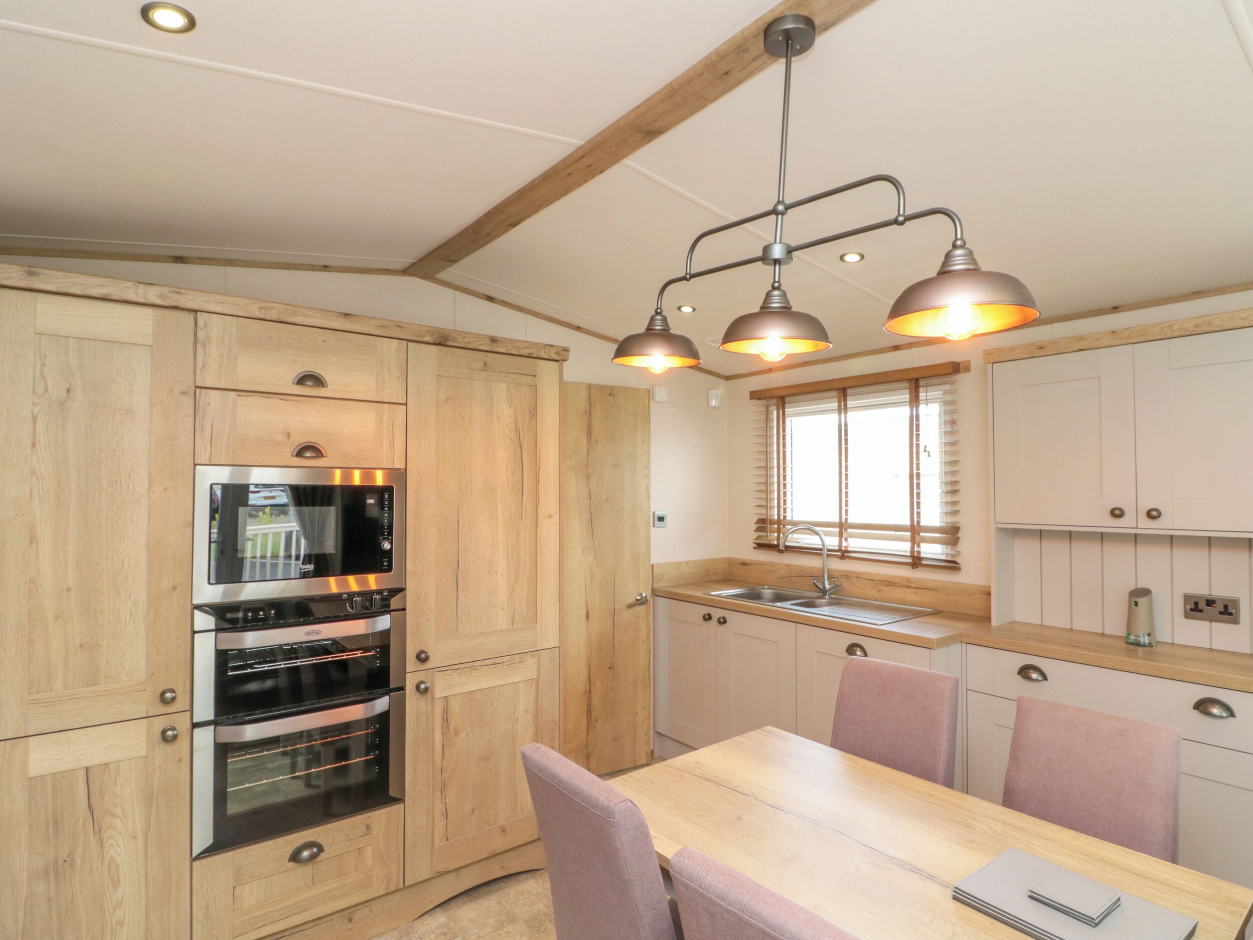 A kitchen with wooden cabinets, a built-in oven, a sink, and pendant lighting.