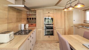 A compact kitchen with wooden cabinetry, a built-in oven, a gas stove, and a dining area with a table and chairs. - Drake 11 (Scarborough)