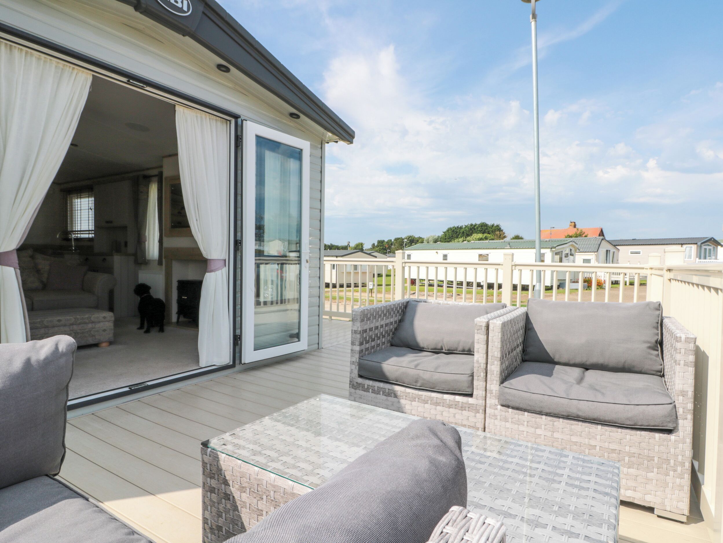 A covered outdoor seating area with wicker furniture and a glass table, leading to a sliding glass door entrance to a room with a sofa and a dog.