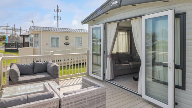 A mobile home with a balcony featuring wicker furniture and a sliding glass door leading to a living area. - Drake 11 (Scarborough)