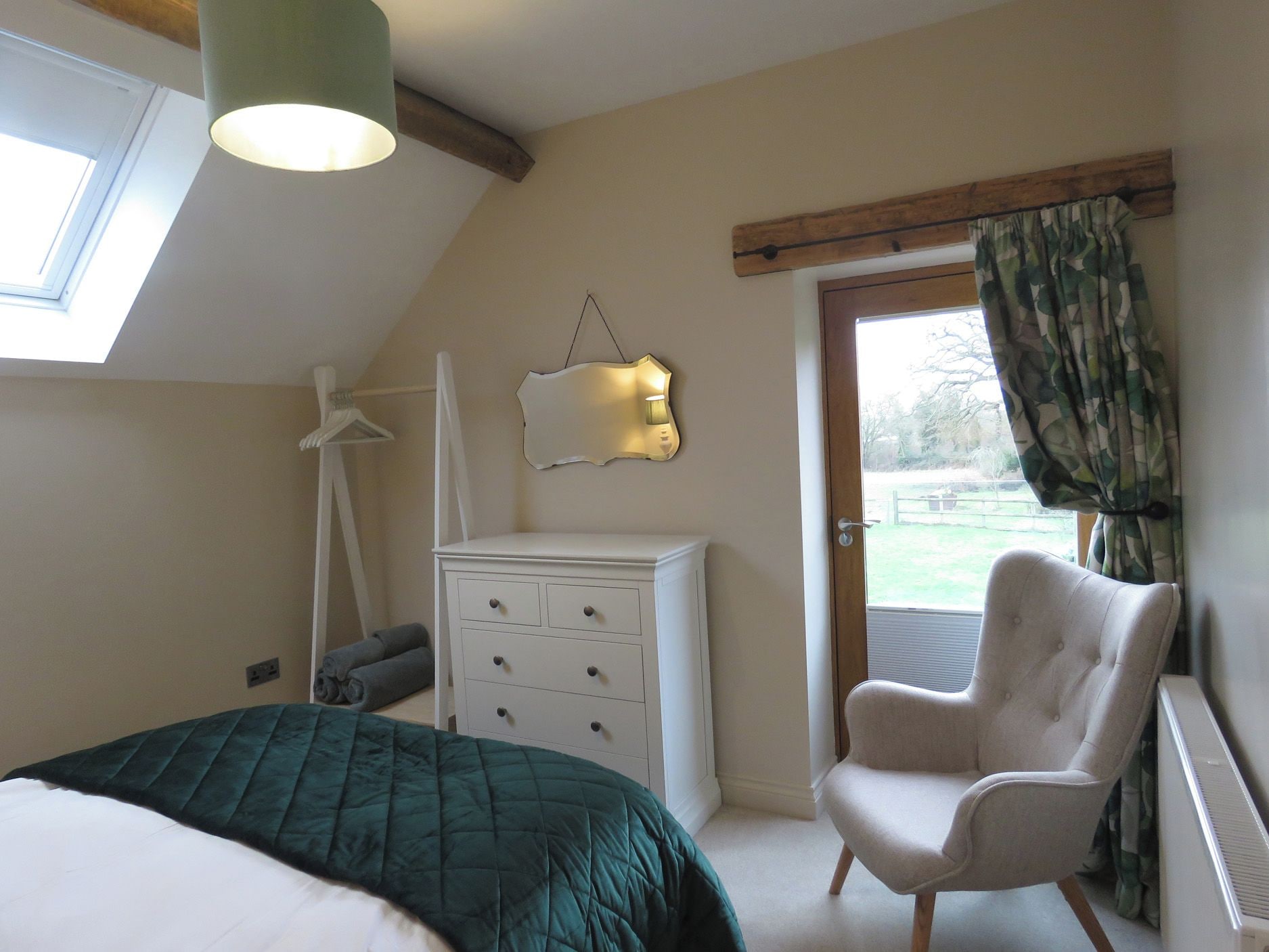 A bedroom with a bed, a dresser, a chair, a hanging lamp, and a window with curtains.