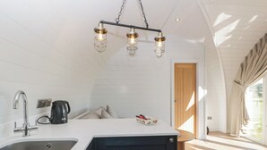 Una cucina dal design moderno, con una grande isola centrale dotata di lavello e bollitore. Si nota una porta in legno e una finestra con tende.