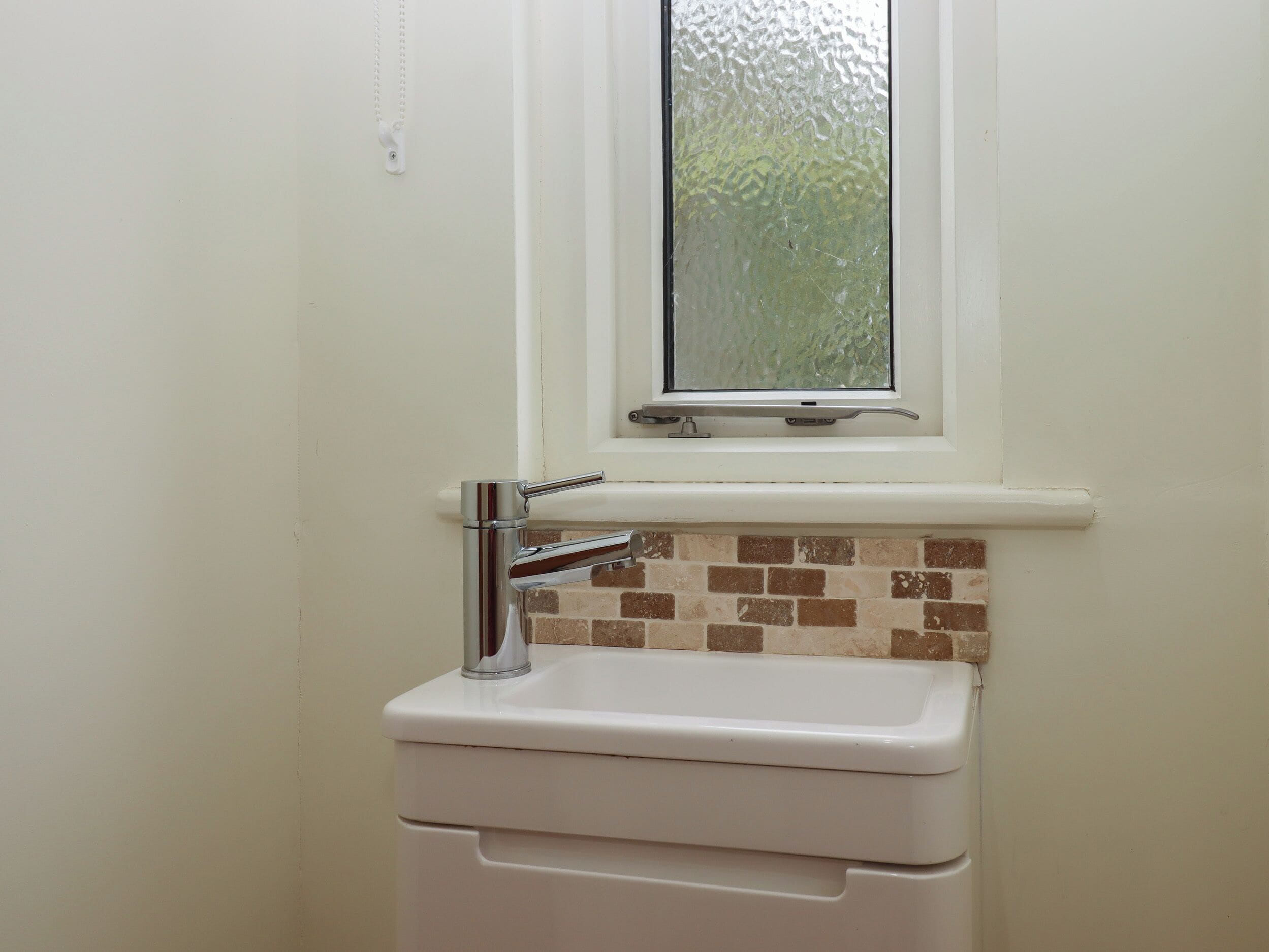 A bathroom with a white sink, a window above it, and a tiled backsplash.