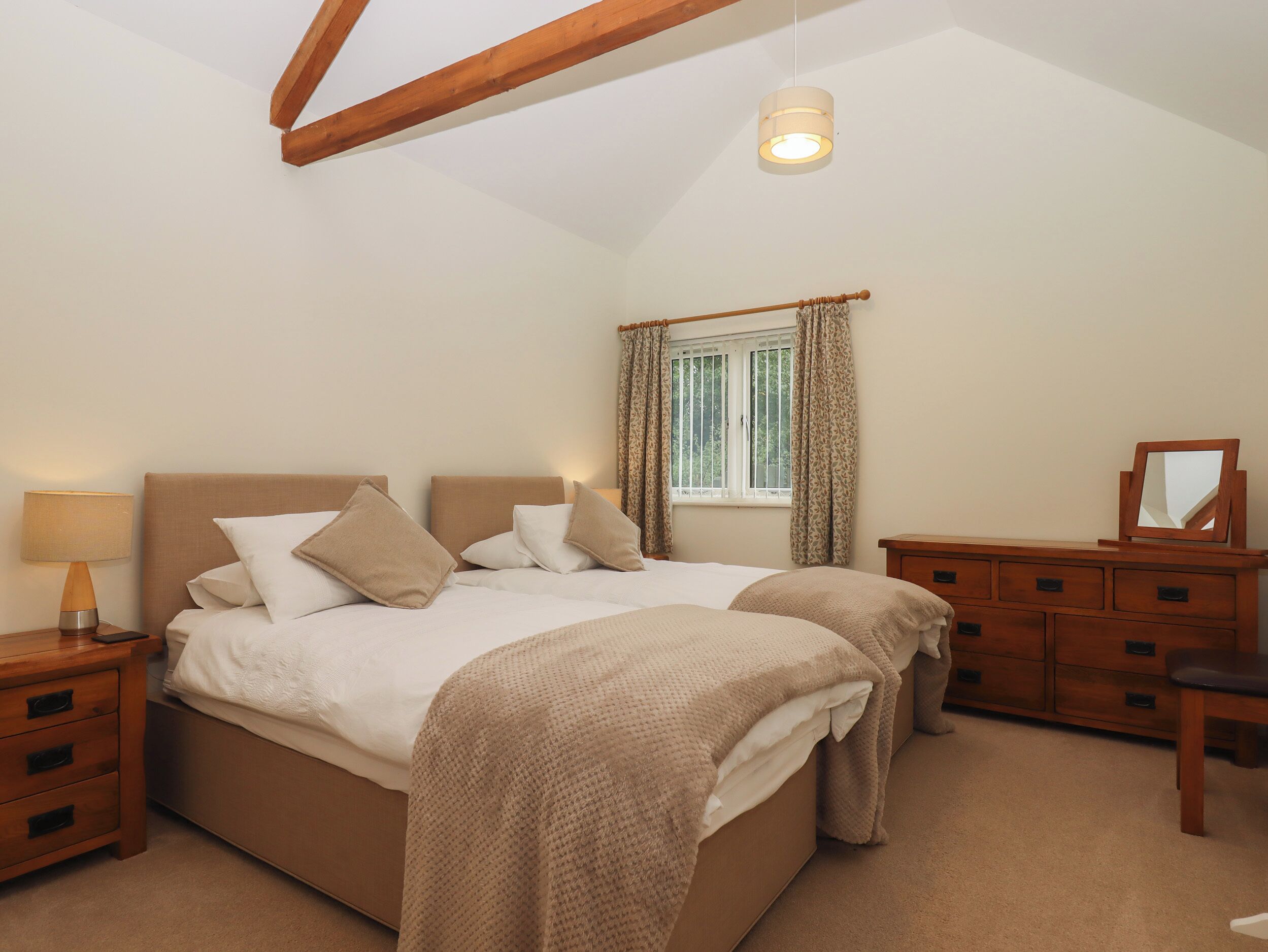 A bedroom with a large bed, wooden nightstands, a dresser, and a window with curtains.