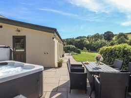Un patio con jacuzzi, mobiliario exterior y vistas a un jardín.