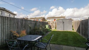A backyard with a metal table and chairs, a wooden fence, a shed, and a well-maintained lawn. - 25 Resbury Close (Cambridge)