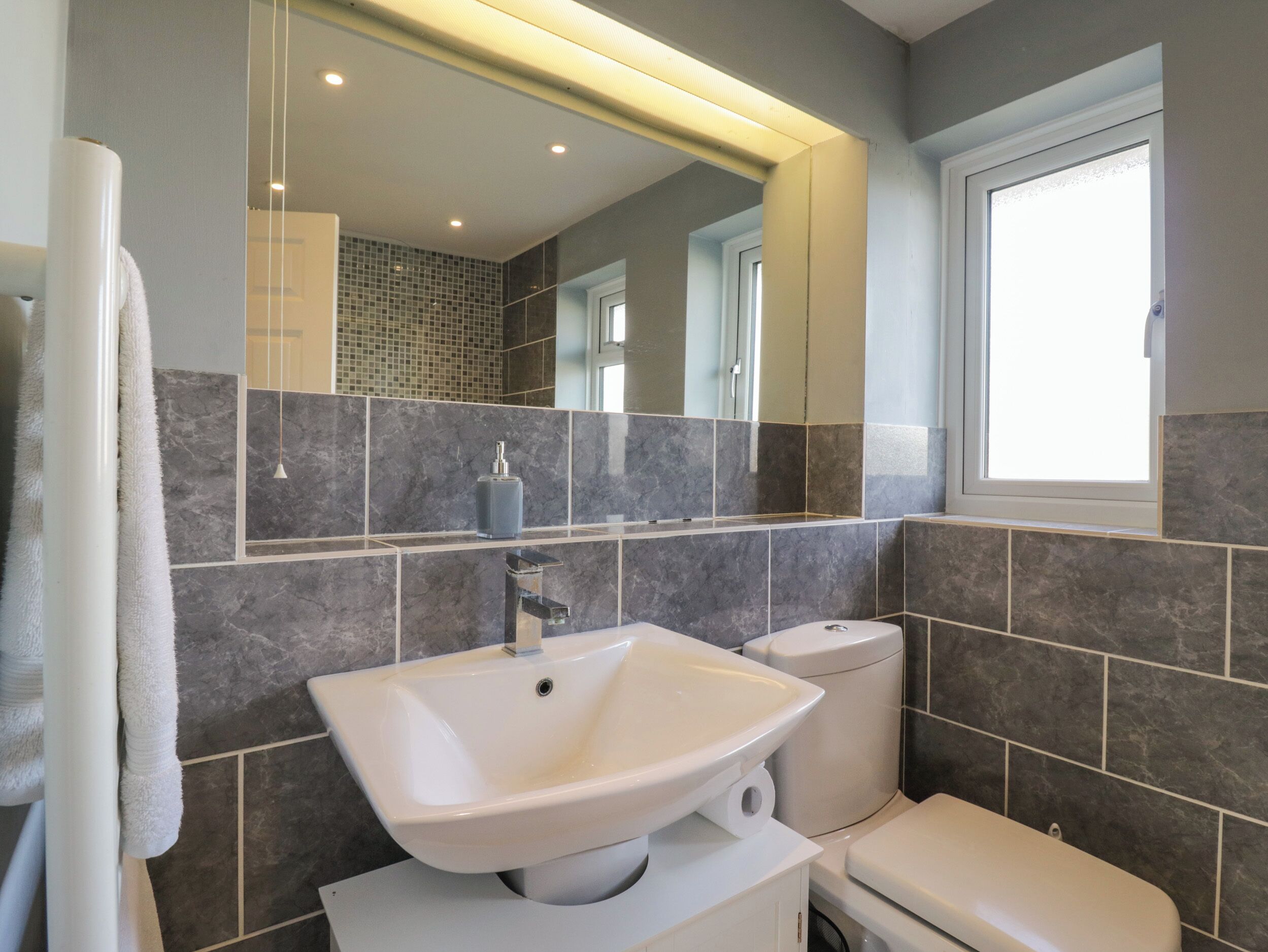 A modern bathroom with a large mirror, a white sink, and a toilet.