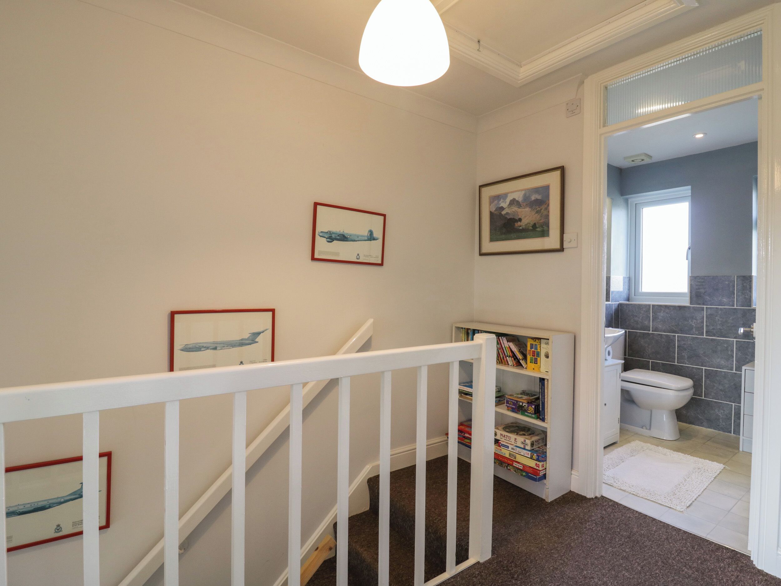 A staircase with white railings leading to a landing with framed pictures and a bookshelf.
