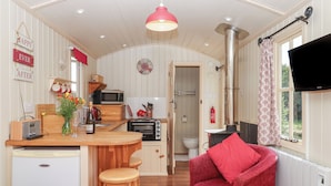 A cozy kitchen with wooden counters, a microwave, a toaster, and a sink. There is a red chair and a small stool in the dining area.