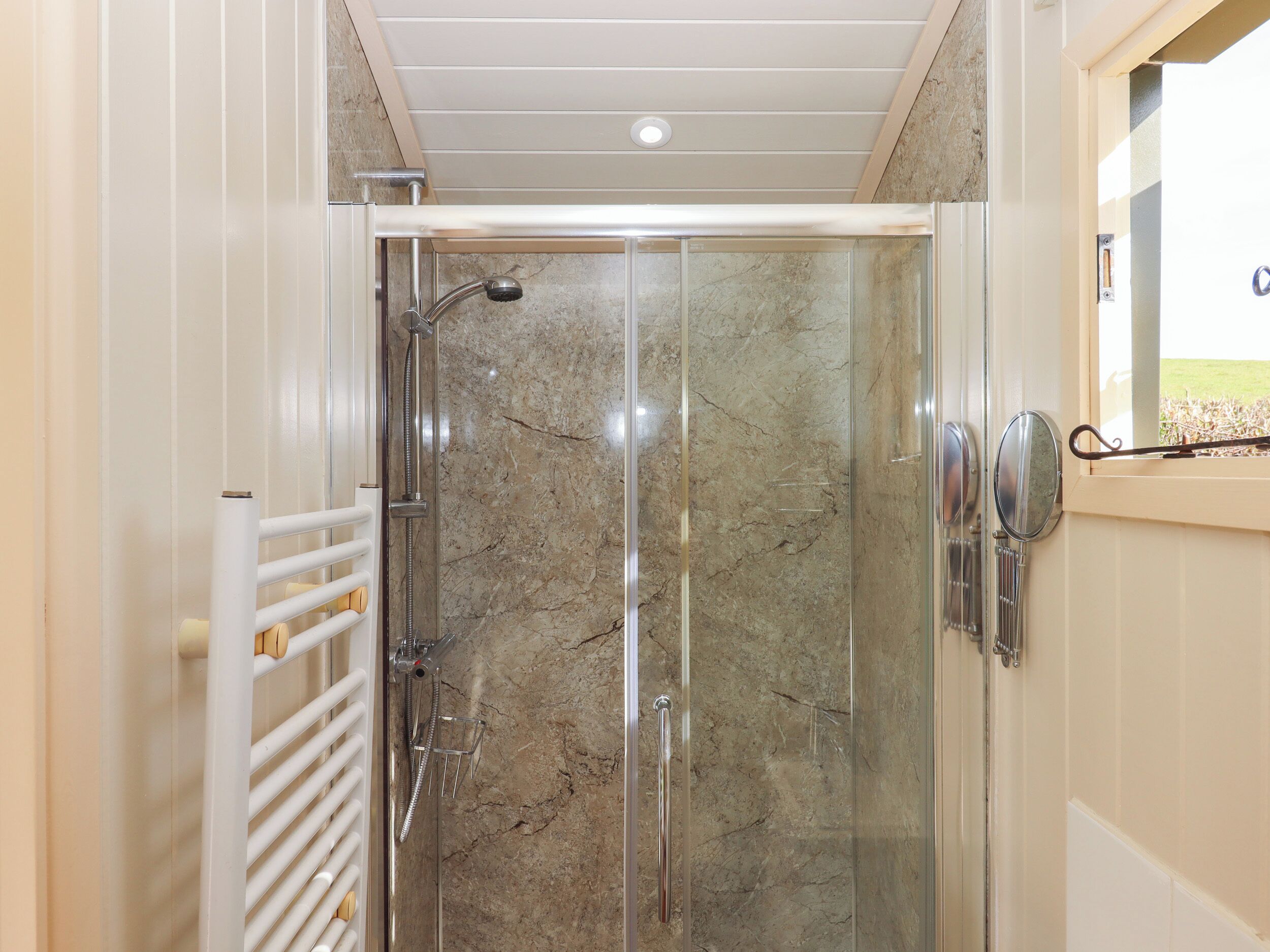 A glass-enclosed shower with a marble wall, a white towel rack, and a door with a handle.
