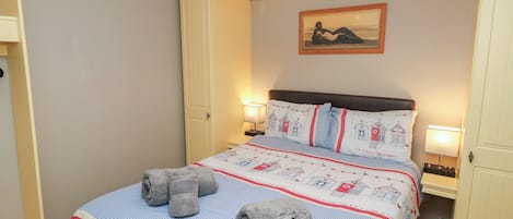 A neatly made bed with a patterned bedspread, two rolled towels, and a wall-mounted picture.