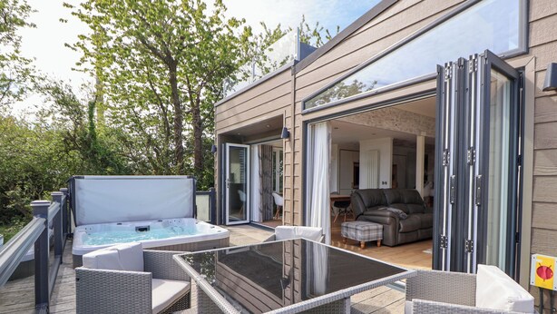 Una terraza al aire libre con jacuzzi, mobiliario de mimbre y una mesa de vidrio.