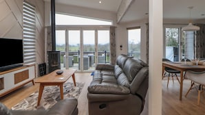 Una sala de estar moderna con un sofá modular, un televisor de pantalla plana, un comedor con mesa y sillas, y puertas de cristal correderas que dan a un balcón.